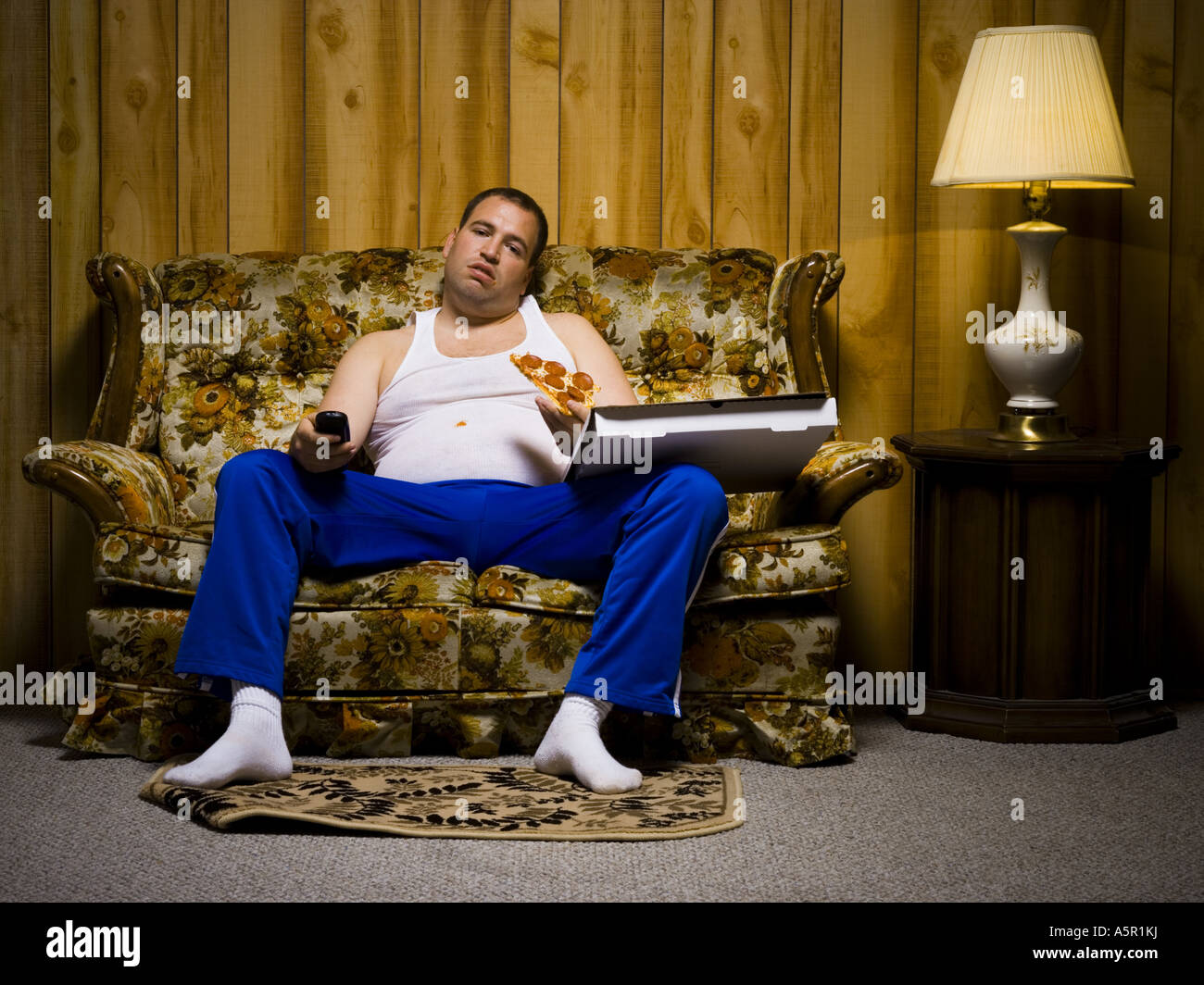 Man on sofa with pizza and TV remote Stock Photo