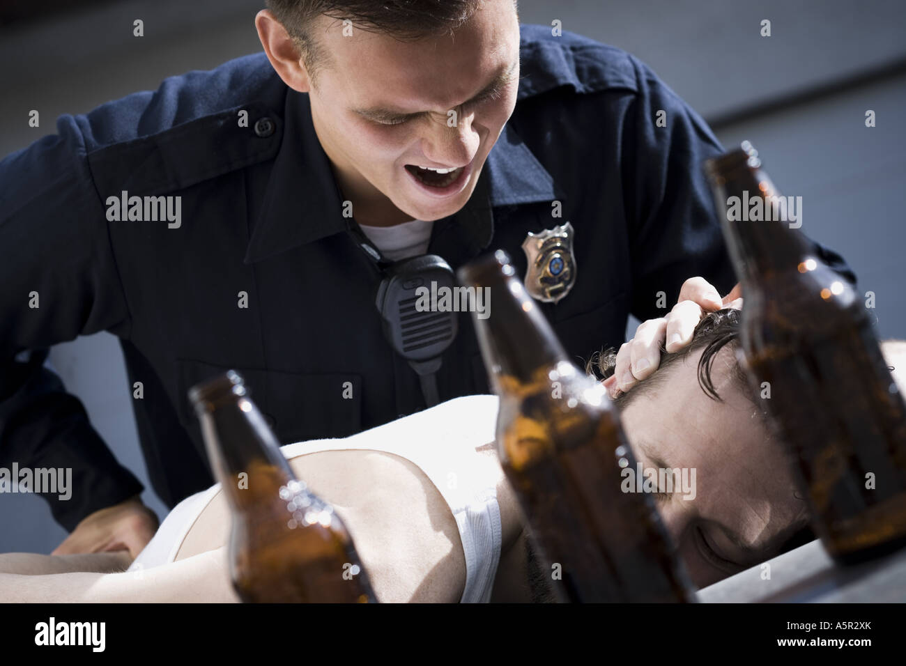 Police officer arresting man lying down with beer bottles Stock Photo