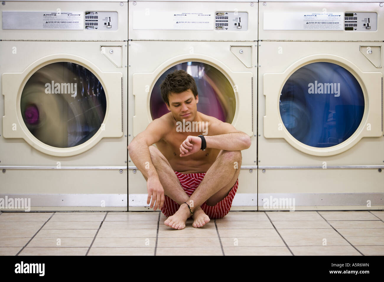 Man sitting in boxers at Laundromat checking watch Stock Photo - Alamy