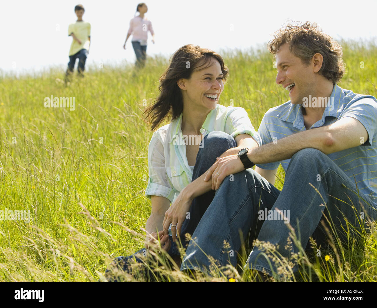 Close up of a woman and a man sitting together and laughing in a field ...