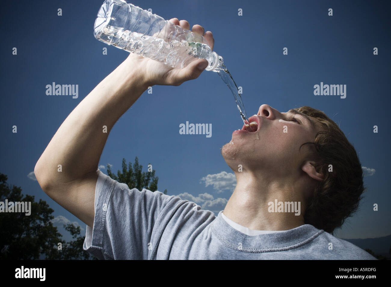 Teen boy wiping his brow and drinking water from a bottle, Stock image