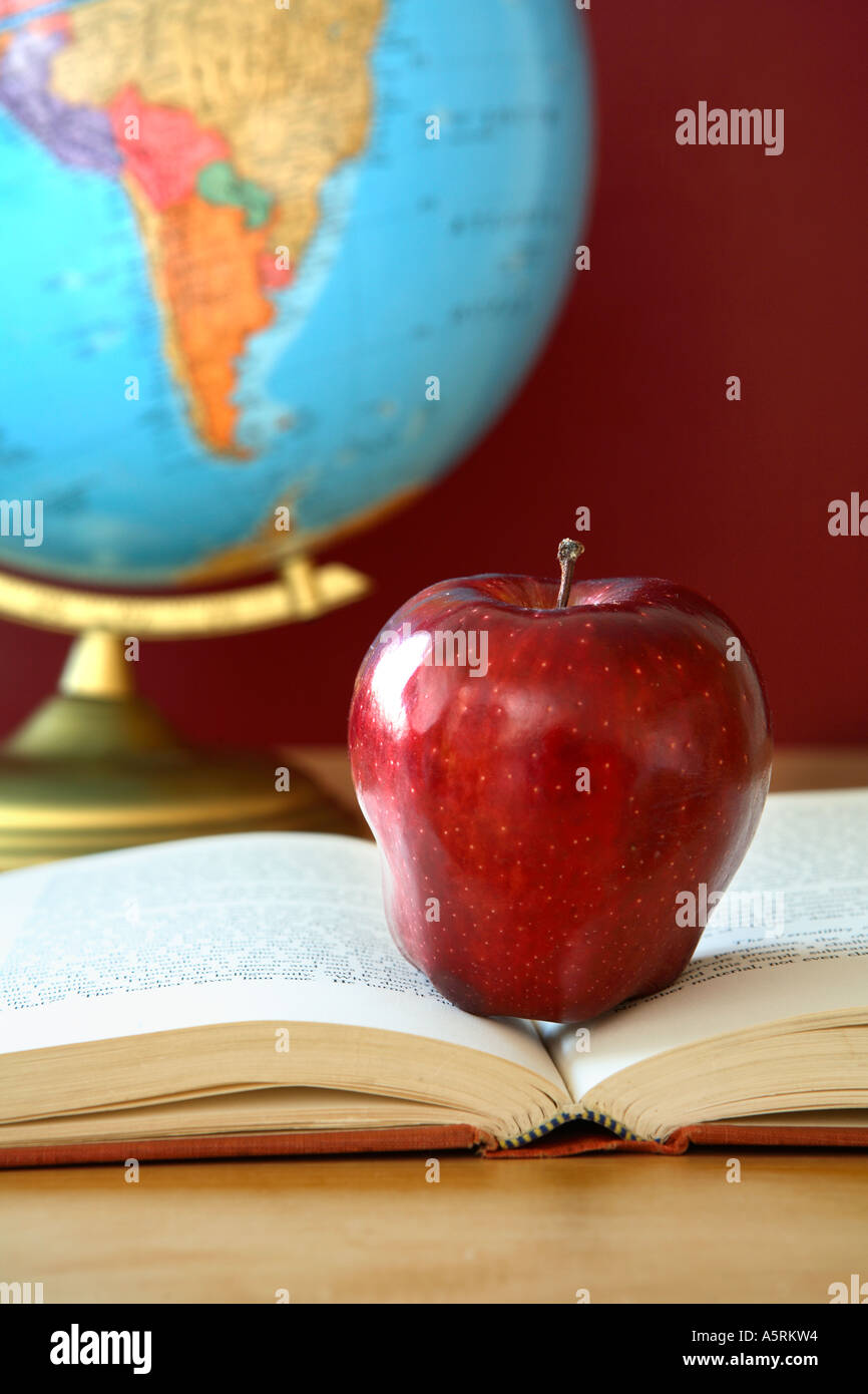 School still life with red apple on open book with globe in background. Stock Photo