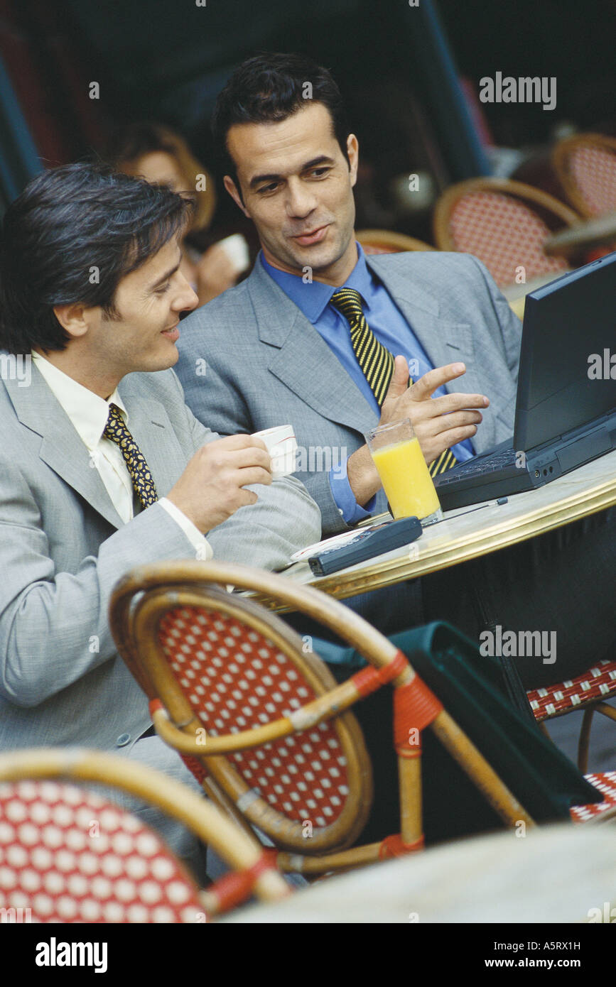 Two businessmen sitting at sidewalk cafe, using laptop Stock Photo