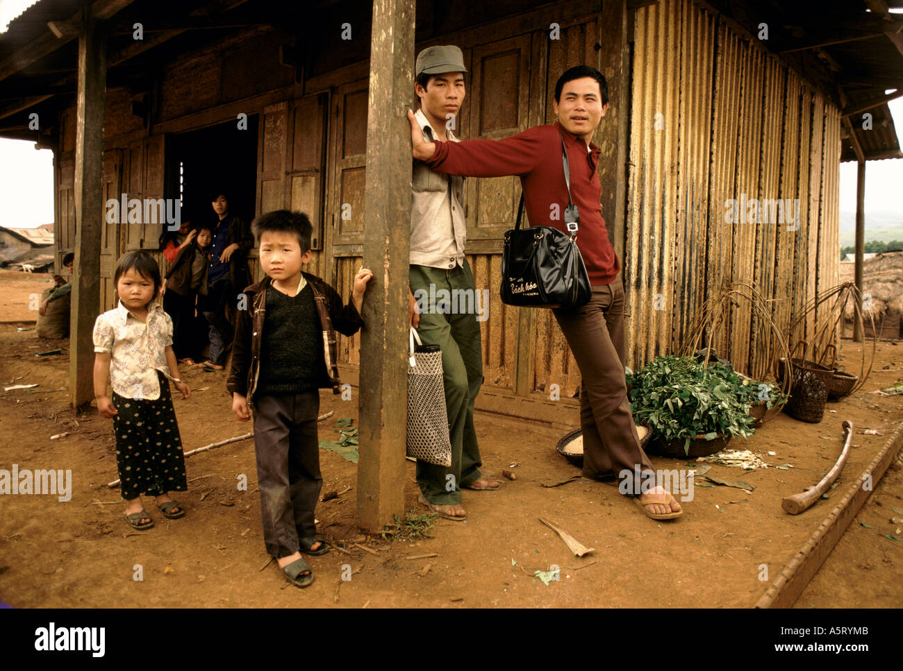 VIETNAM,  LOCALS WITH YOUNG CHILDREN OUTSIDE THEIR VILLAGE HUT WITH BASKETS OF VEGETABLES Stock Photo