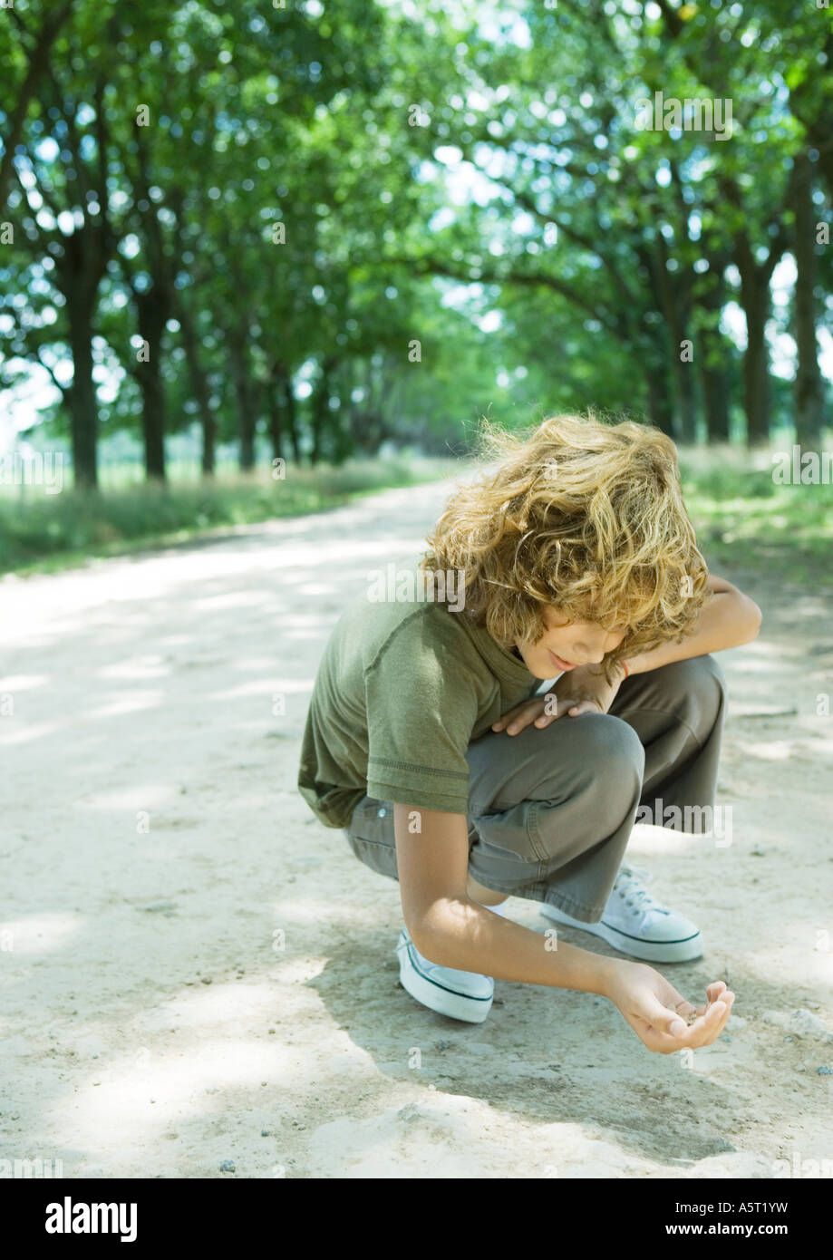 Boy crouching in dirt road Stock Photo