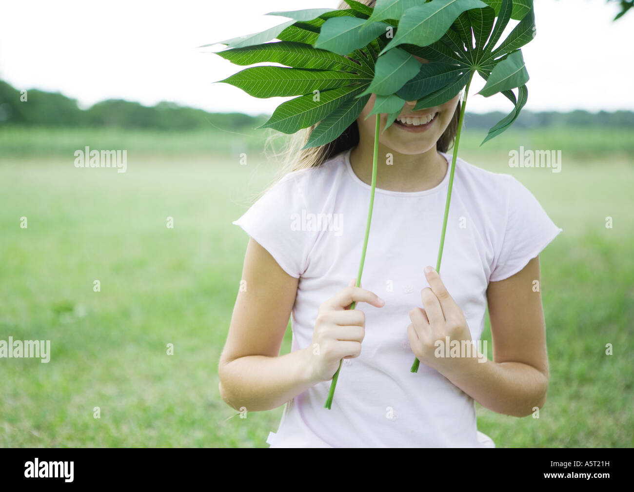 Girl holding up cassava leaves in front of face Stock Photo