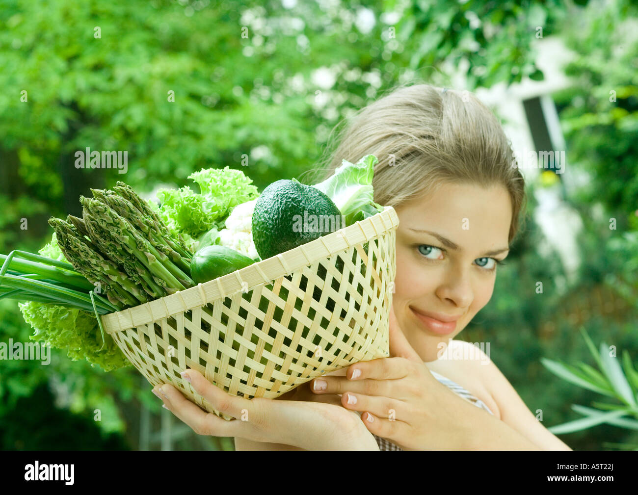 Woman holding basket full of fresh vegetables, smiling at camera Stock Photo