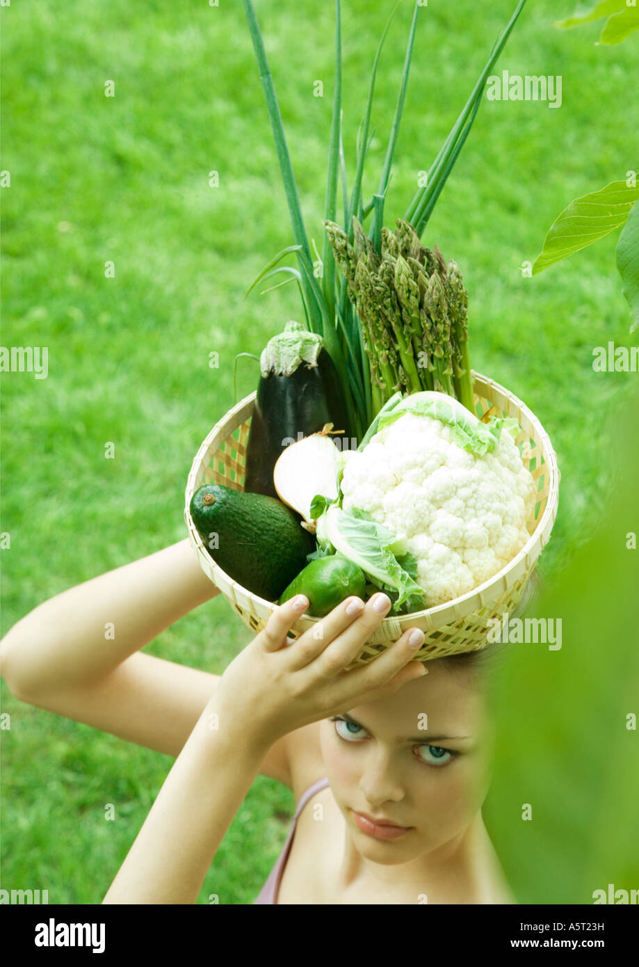 Woman holding basket full of fresh vegetables on top of head Stock Photo