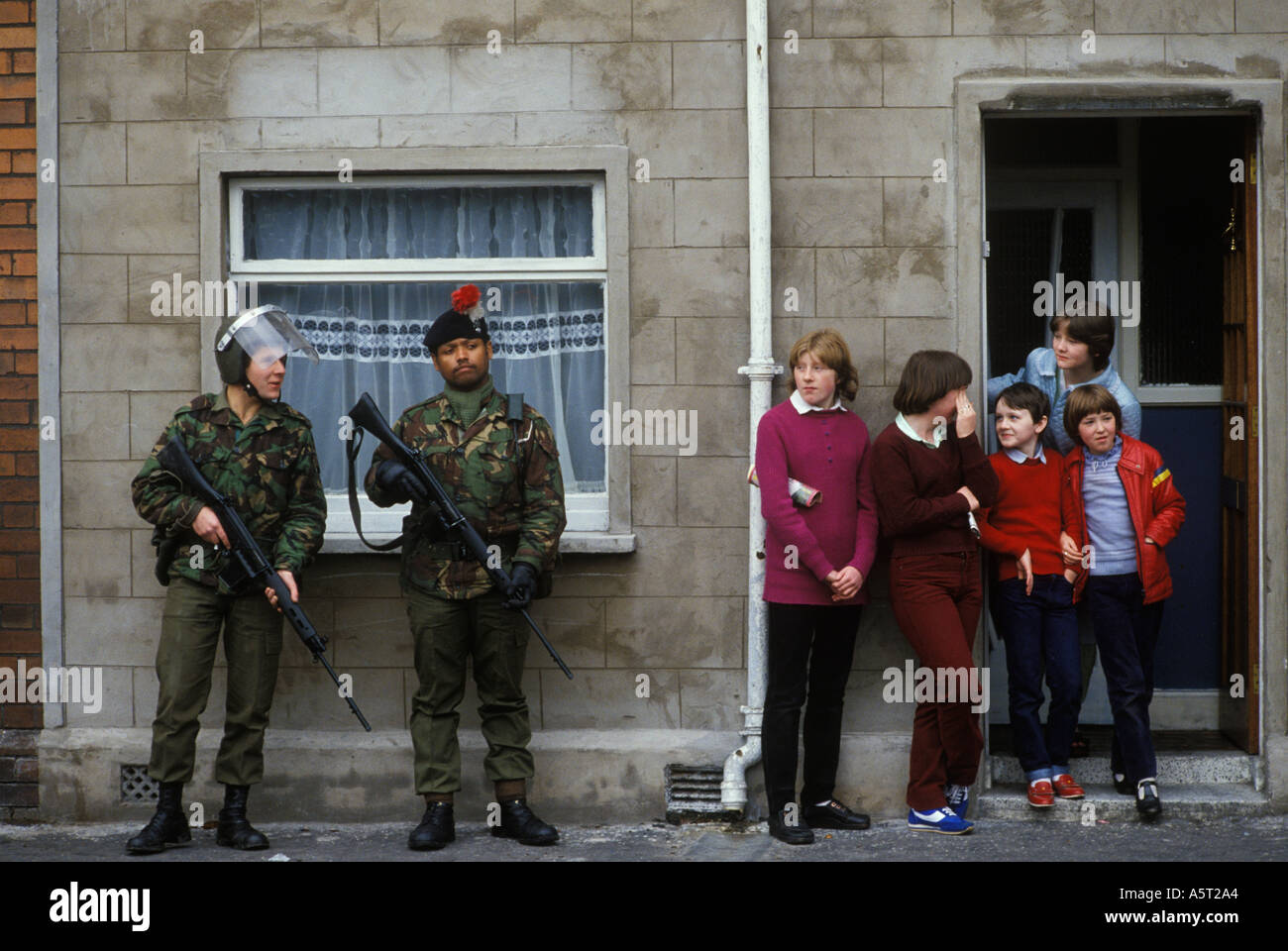 The Troubles 1980s British troops black British army soldier on foot patrol in Belfast. Multi ethnic and armed, family mother children daily life 1981 Stock Photo