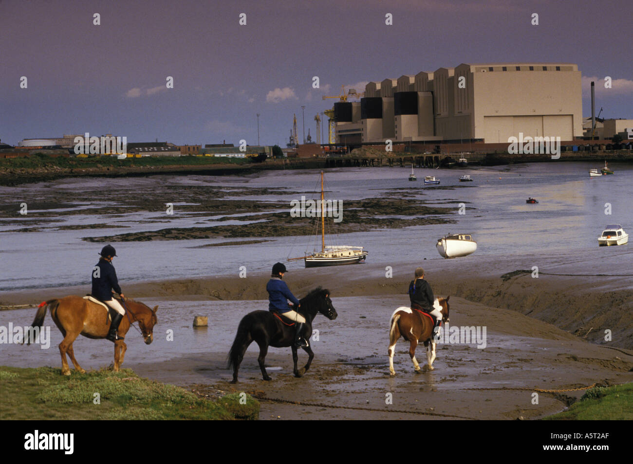 Children on ponies horses with shipyard in  Barrow in Furness Cumbria. Taken from Walney Island across Walney Channel. UK 1980s 80s HOMER SYKES Stock Photo