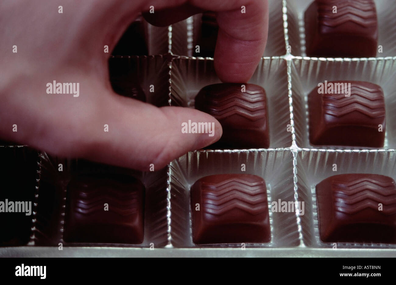 Hand picking from a box of chocolates Stock Photo