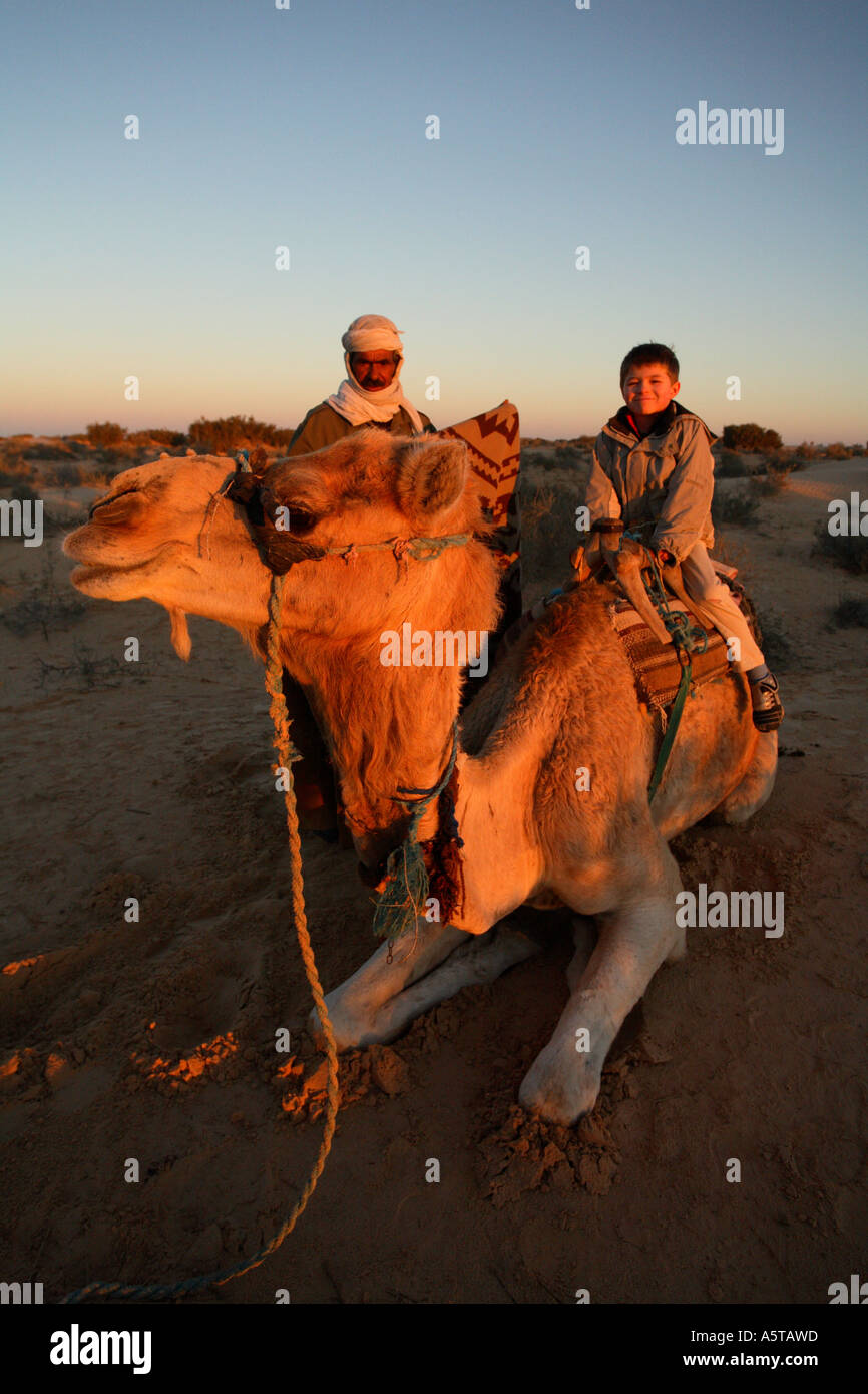 Vertical portrait of young boy tourist riding camel at sunrise, Sahara ...