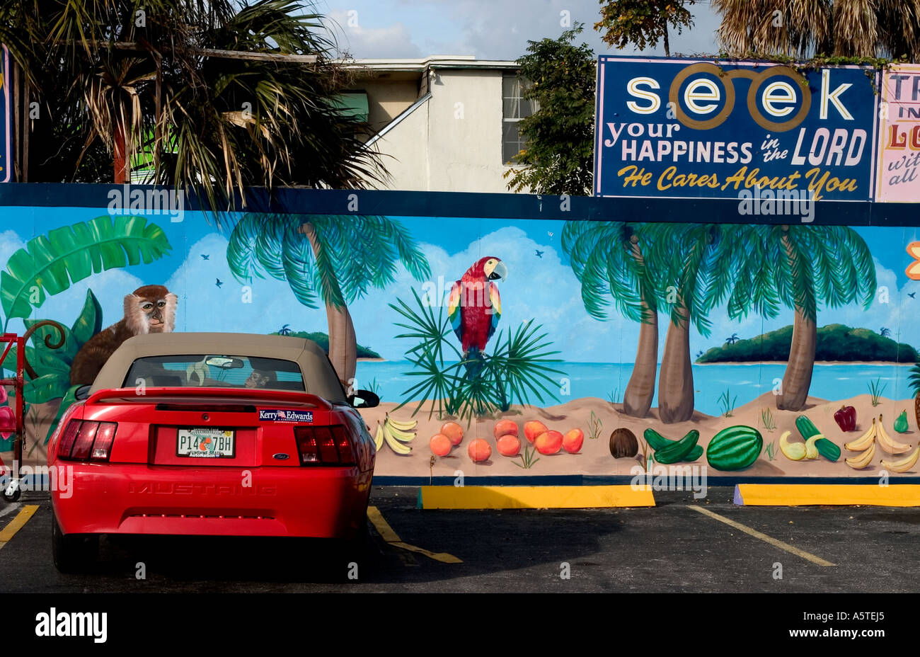 A sporty red Ford Mustang convertible is parked near a mural and sign urging people to seek happiness in the Lord. Stock Photo