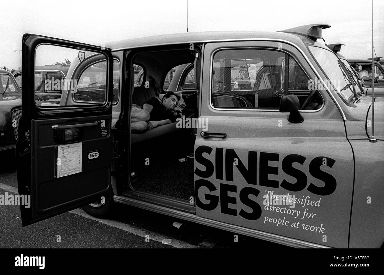 A London taxi driver sleeping in the back of his cab at the feeder park for Heathrow Airport. Stock Photo