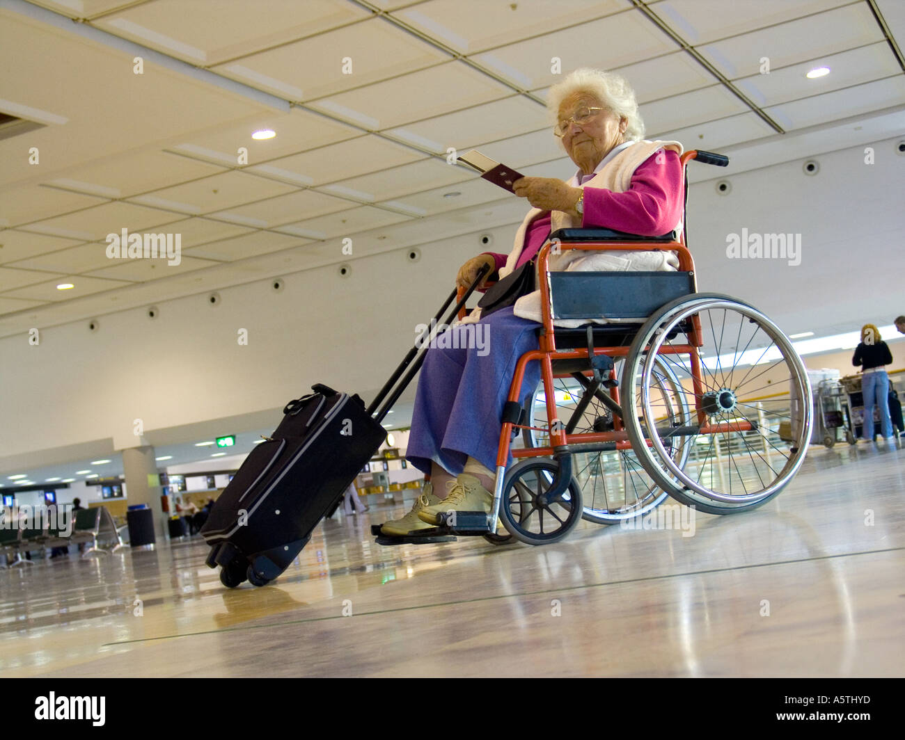 AIRPORT WHEELCHAIR Independent elderly woman waiting on airport concourse checking her tickets