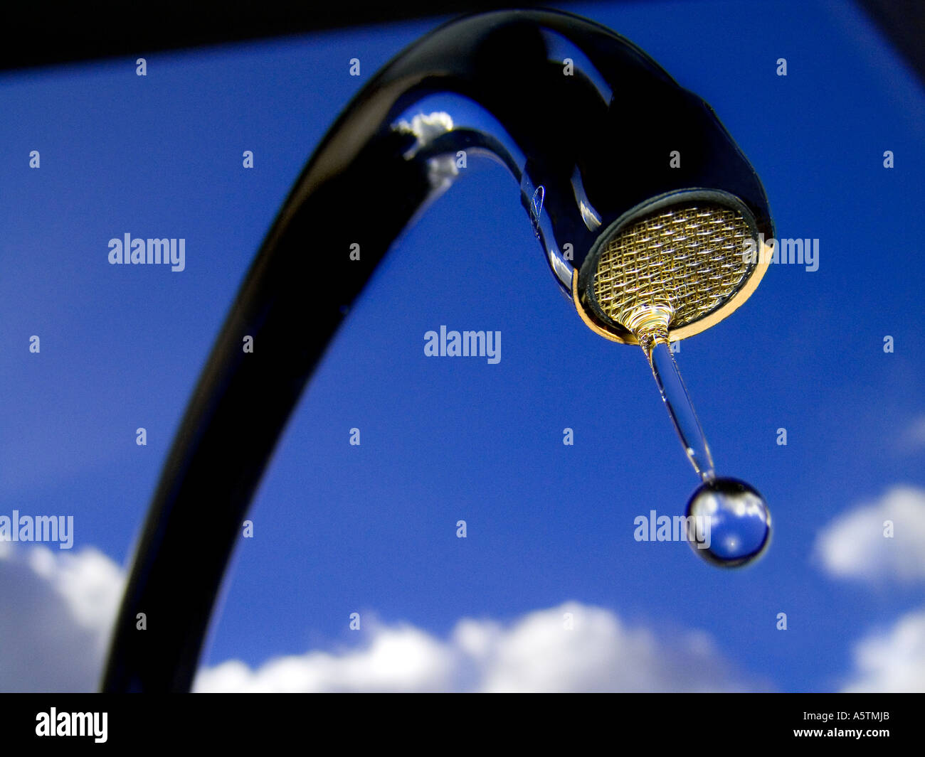 WATER DRIP DROP TAP SKY ENVIRONMENT Clear water droplet from kitchen tap viewed at low angle against bright blue sunny sky and clouds Stock Photo