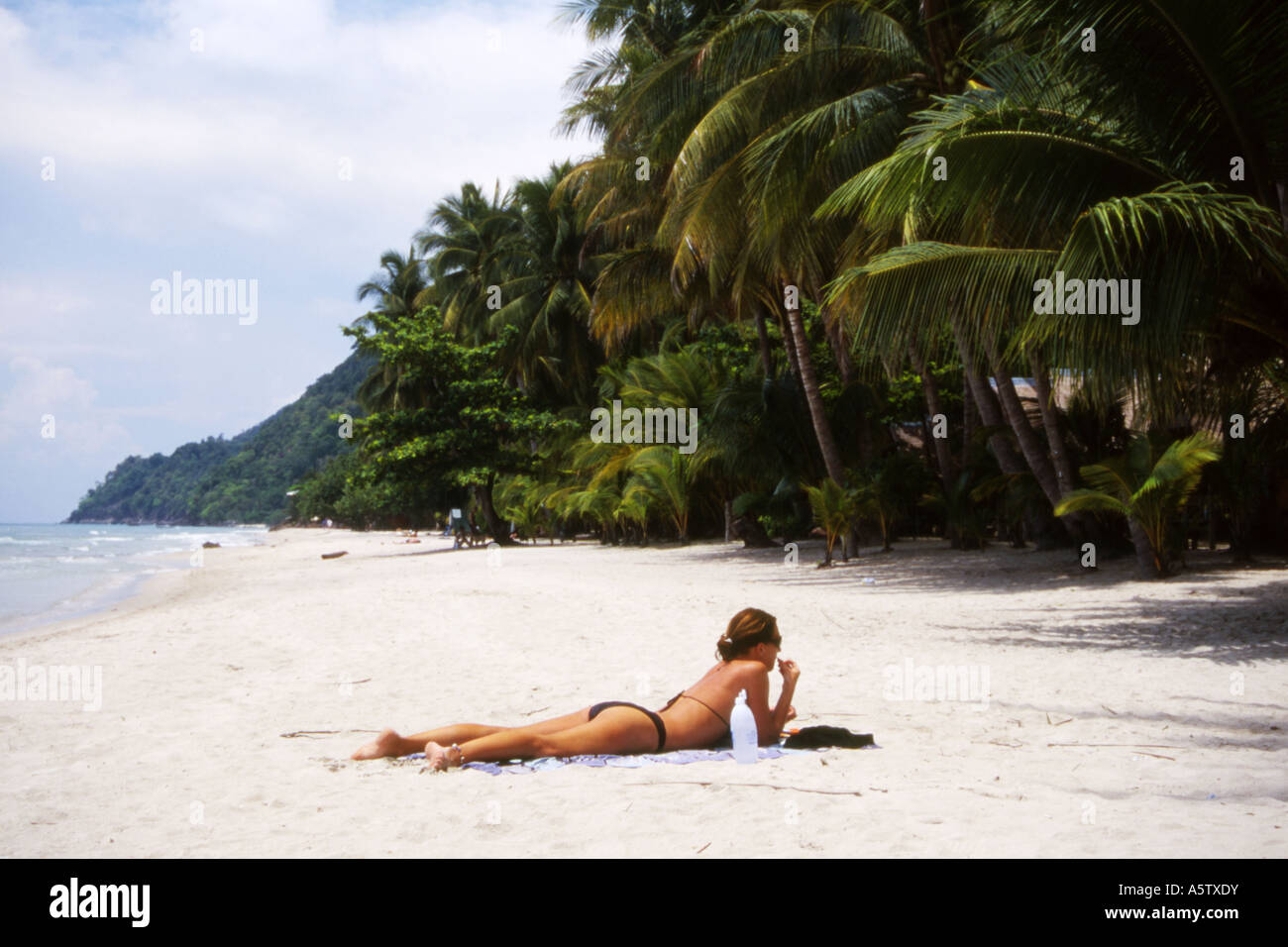 Slim western female tourist sunbathes on a deserted beach edged with palm trees,Koh Chang,Thailand. Stock Photo