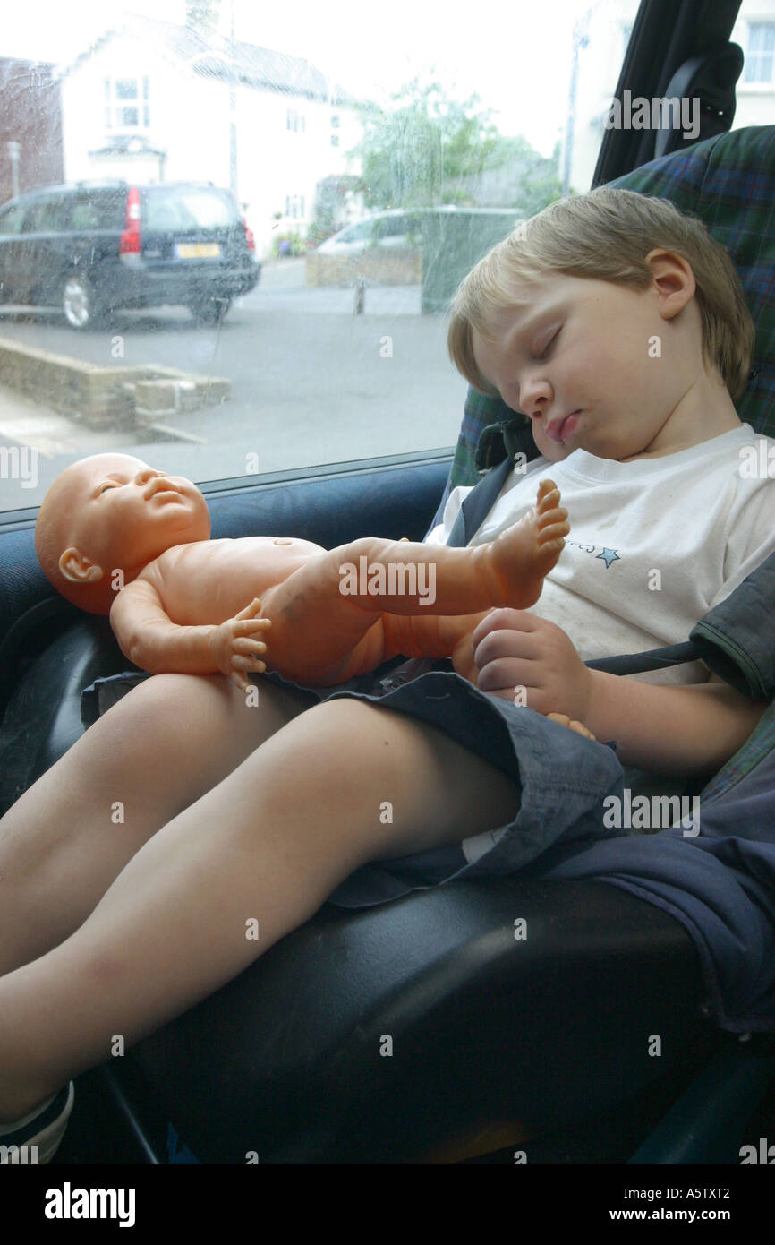 three year old boy sleeping in car seat holding a toy doll Stock Photo