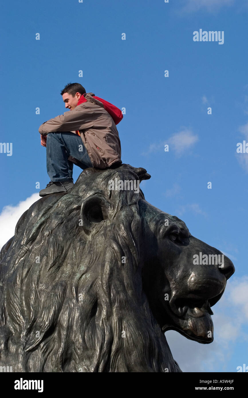 Male tourist sitting on Landseer Lion statue. Trafalgar Square, London, England Stock Photo