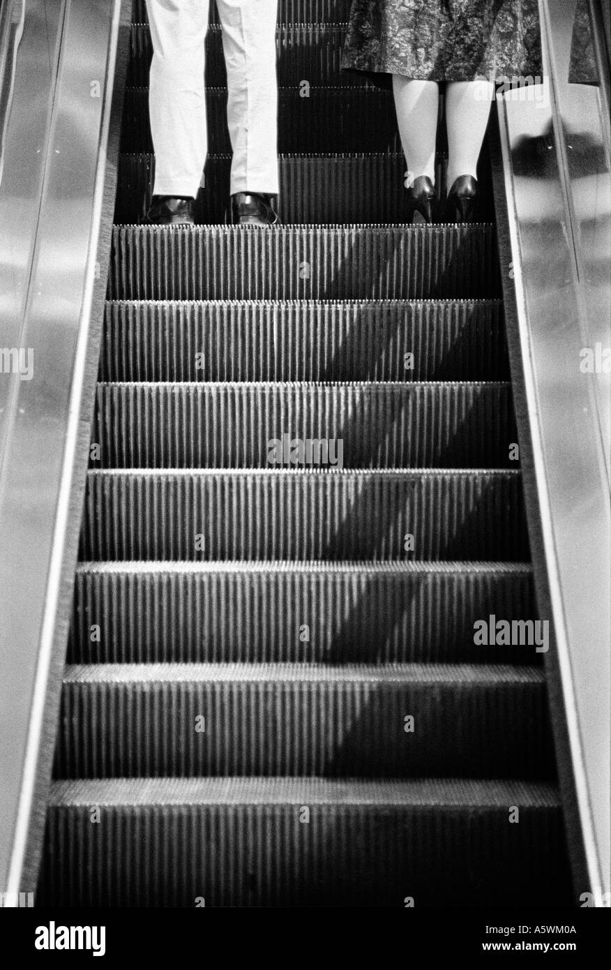 Amusing black and white photo of legs of a couple going up an escalator Stock Photo