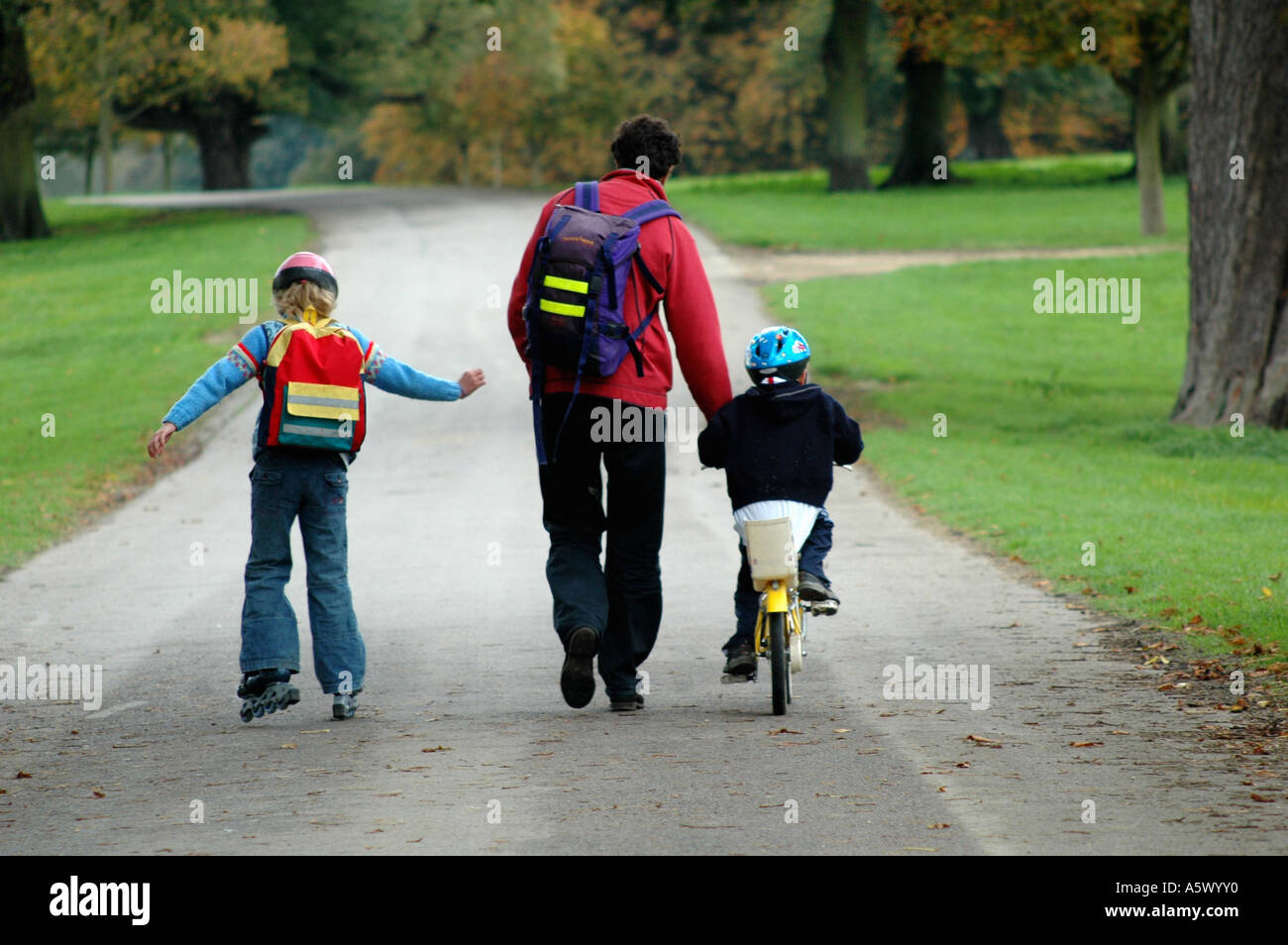 Father in the park with children, one child cycling and one child roller blading Stock Photo
