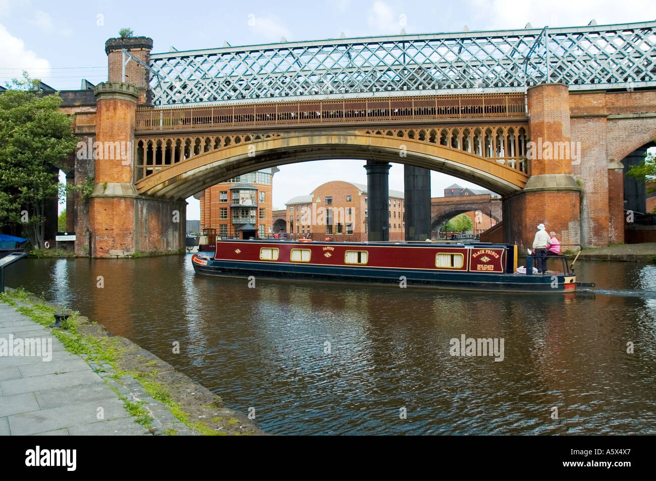 Canal narrowboat beneath a Victorian railway bridge at Castlefield Basin, Manchester, UK Stock Photo
