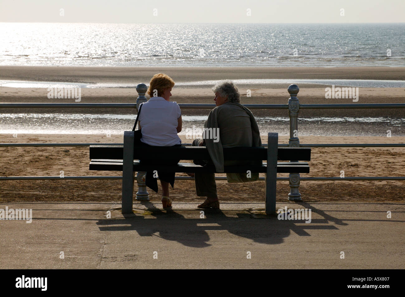 TWO ELDERLY LADIES CHATTING ON BENCH ON GOLDEN MILE BLACKPOOL Stock Photo