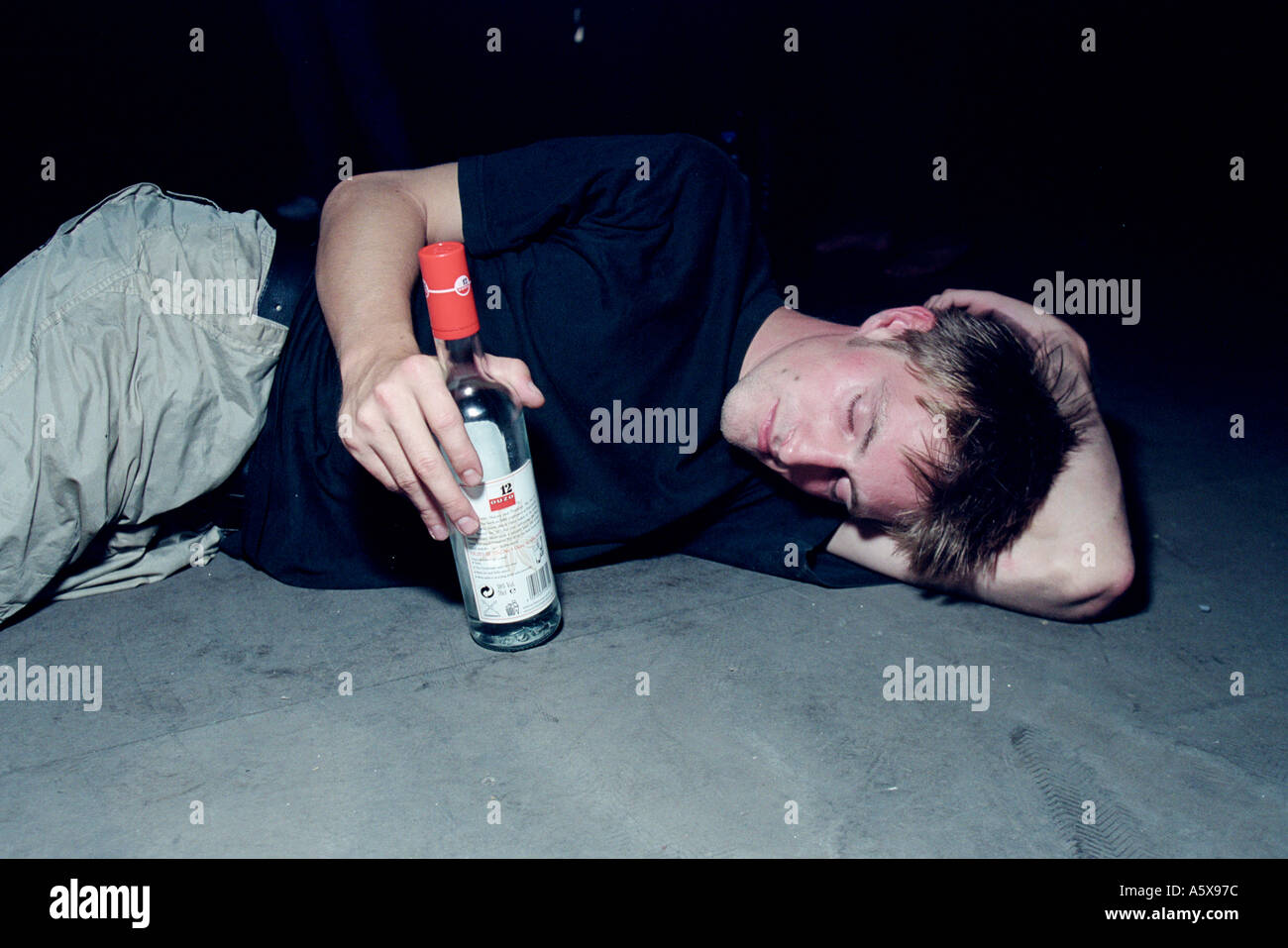 Bloke on floor with bottle of Ouzo at Pulse 8 illegal rave in Essex Stock Photo