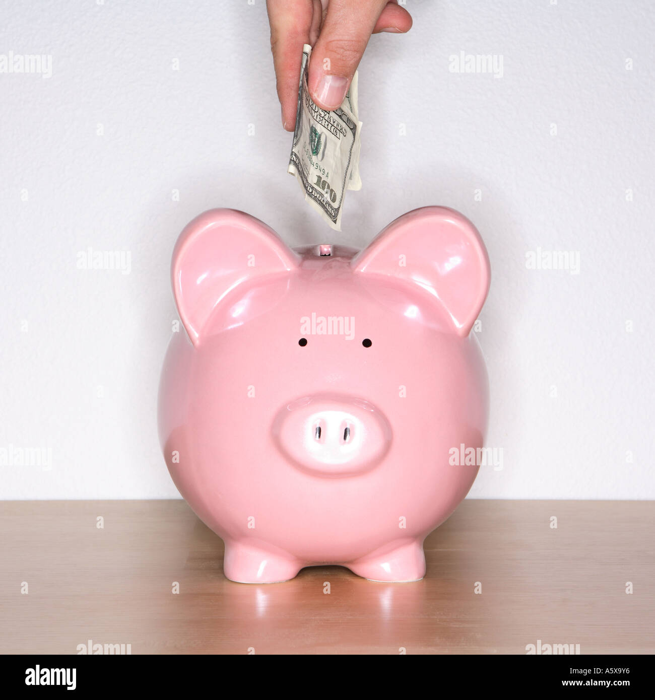 Hand putting 100 dollar bill in pink piggy bank Stock Photo - Alamy
