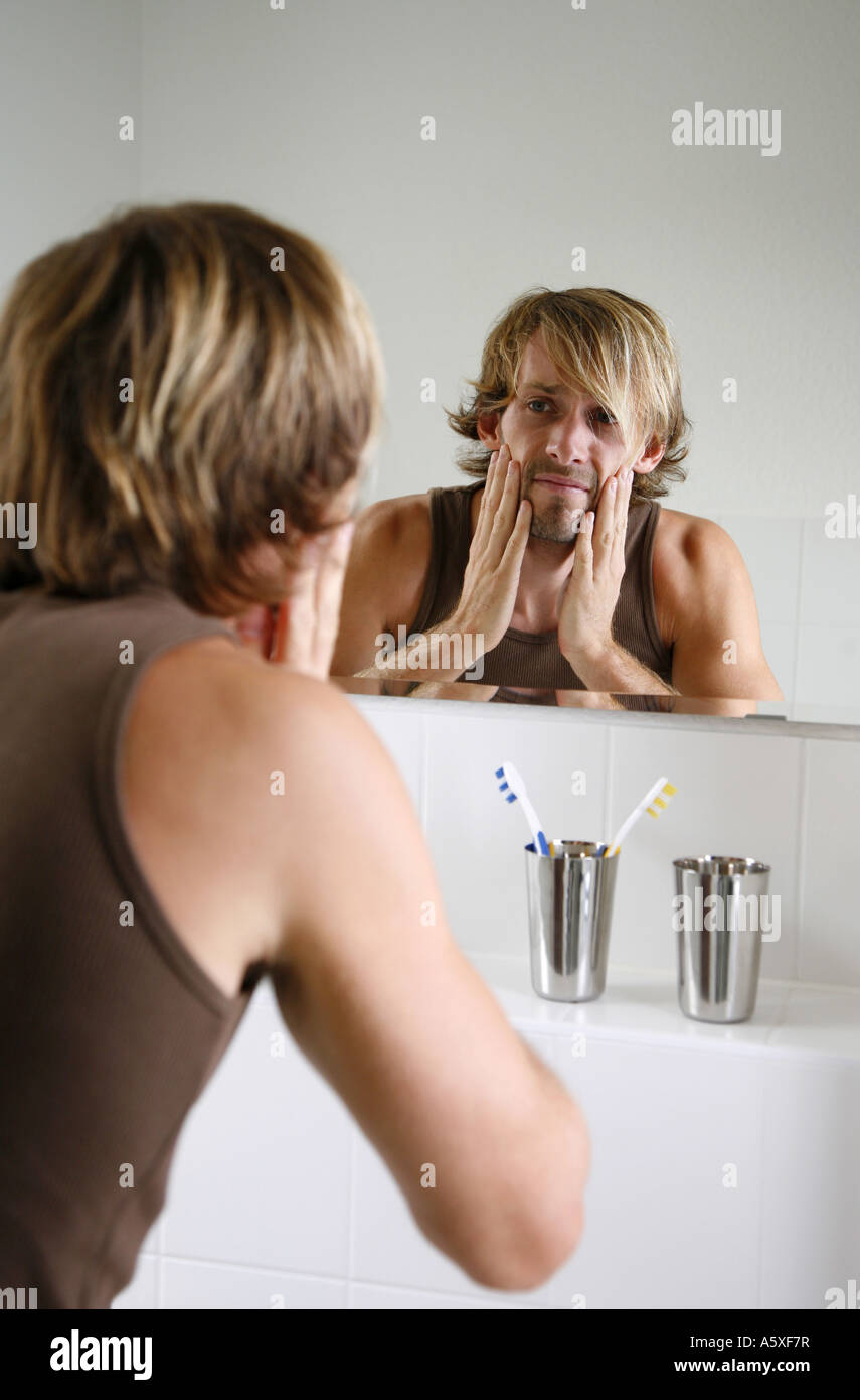 Young man examining face in bathroom mirror close up Stock Photo