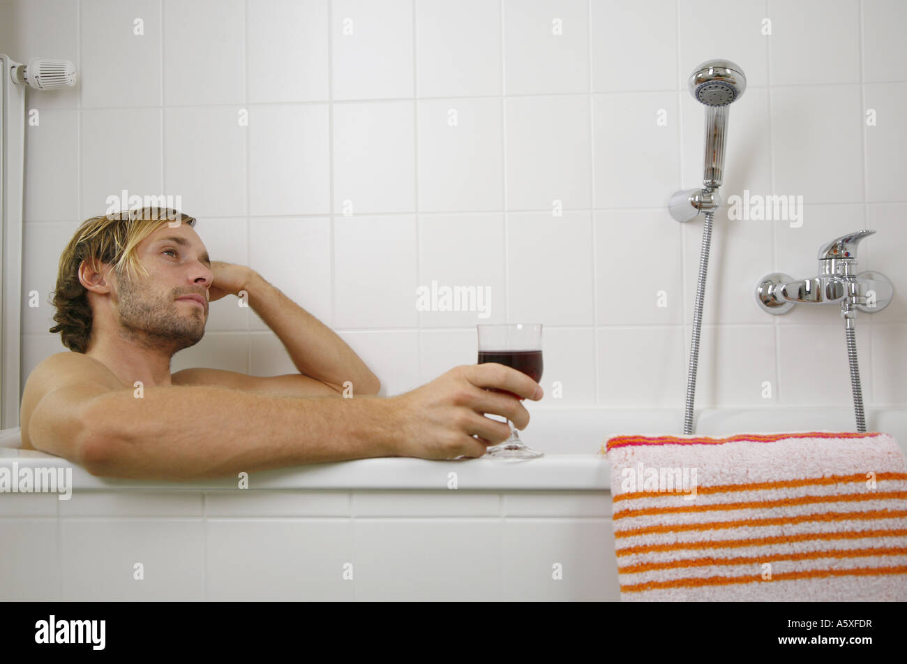 Young man leaning in bath tub holding wine glass close up Stock Photo