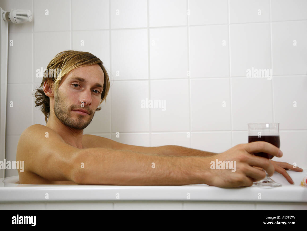 Young man leaning in bath tub holding wine glass close up Stock Photo