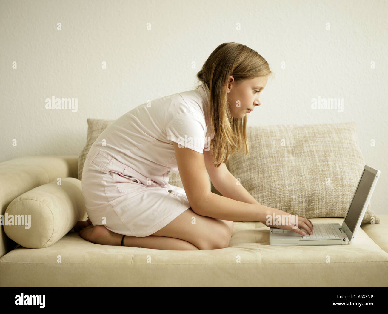 Girl kneeling on sofa and using laptop side view Stock Photo Alamy