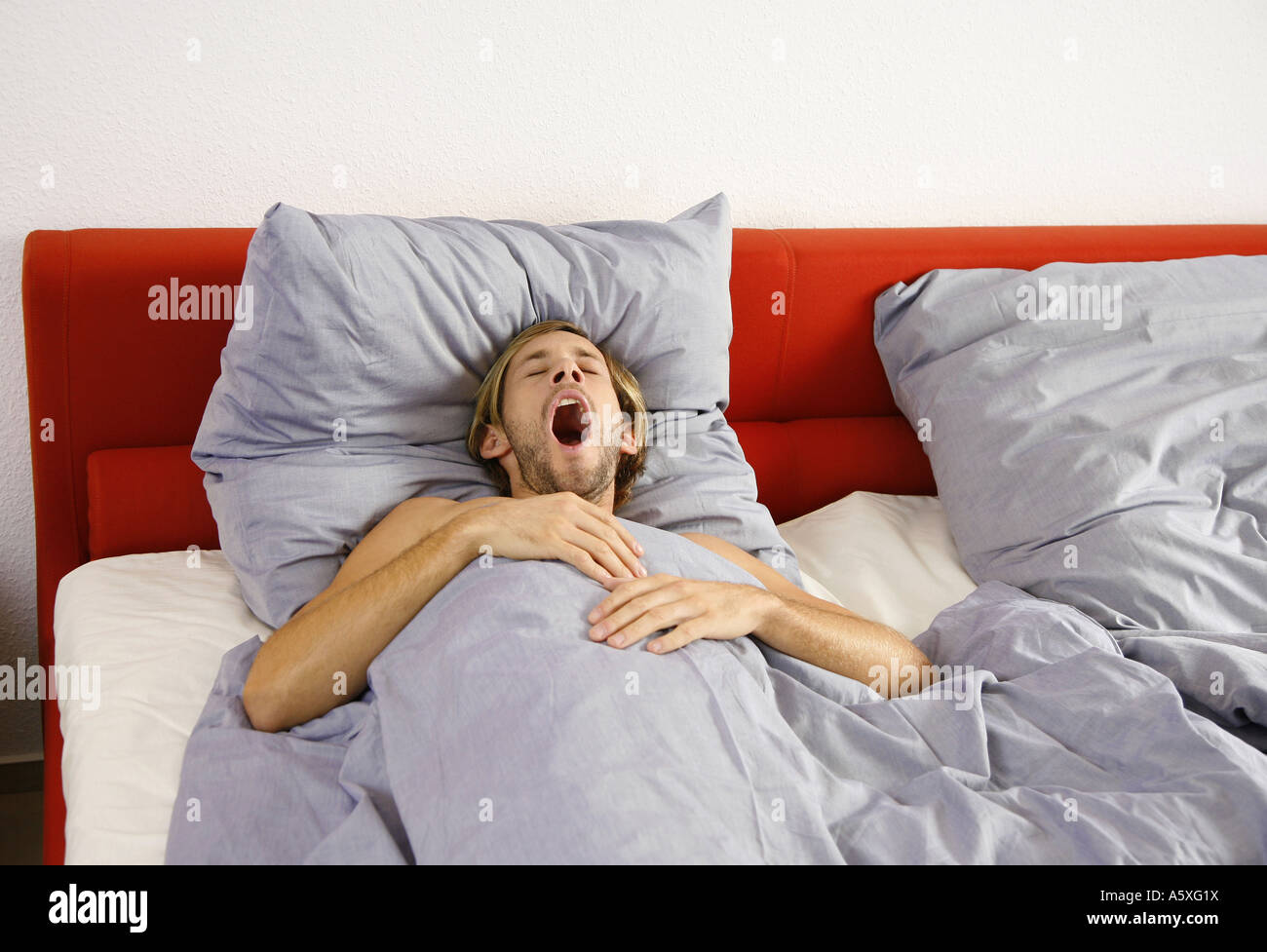 Young man lying on bed yawning elevated view Stock Photo