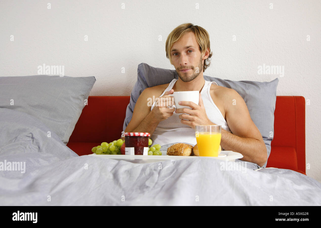 Young man having breakfast on bed smiling portrait Stock Photo