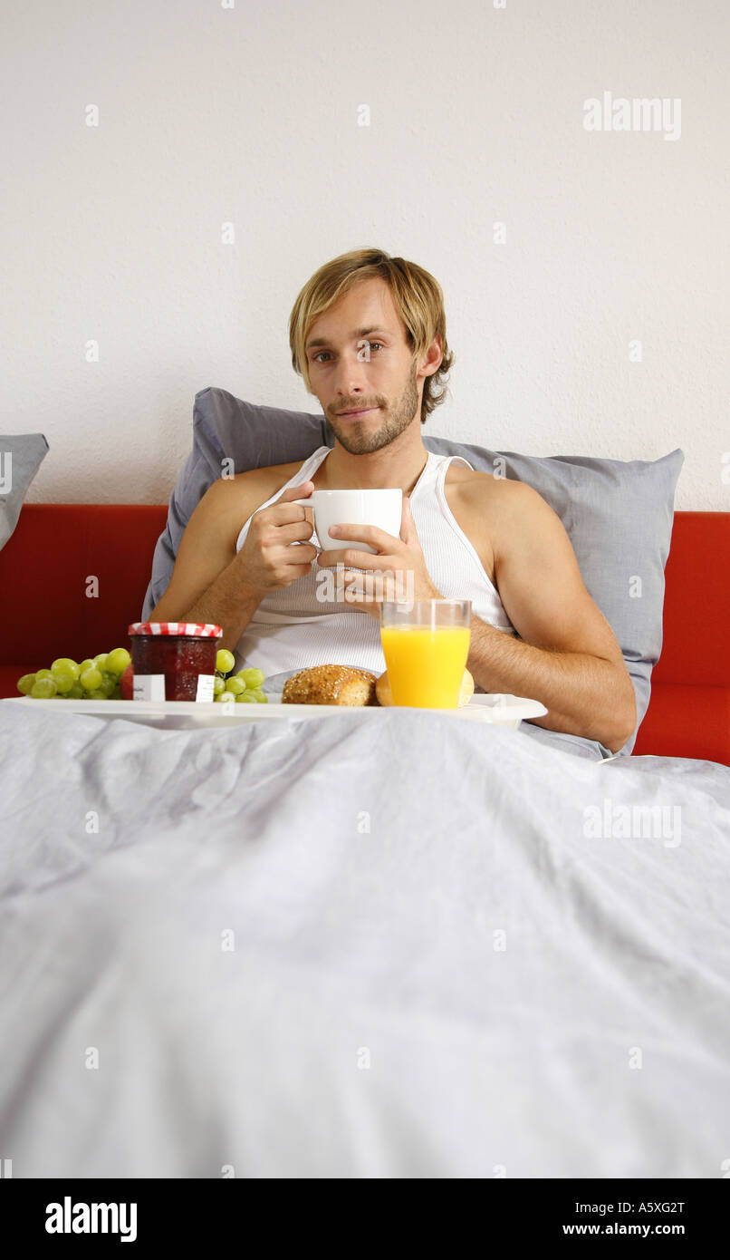 Young man having breakfast on bed smiling portrait Stock Photo