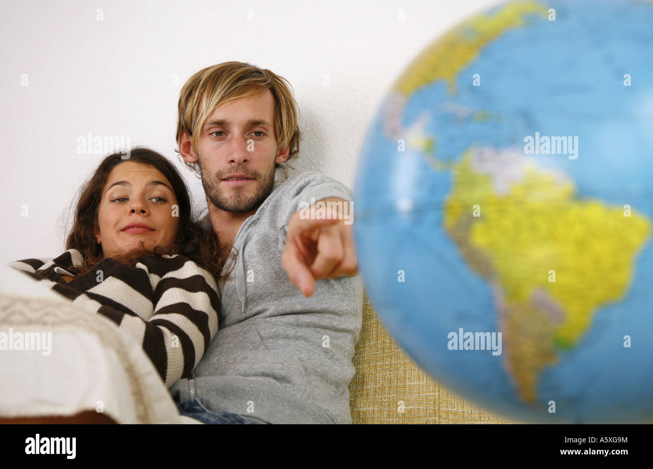 Young couple on couch man pointing at globe Stock Photo
