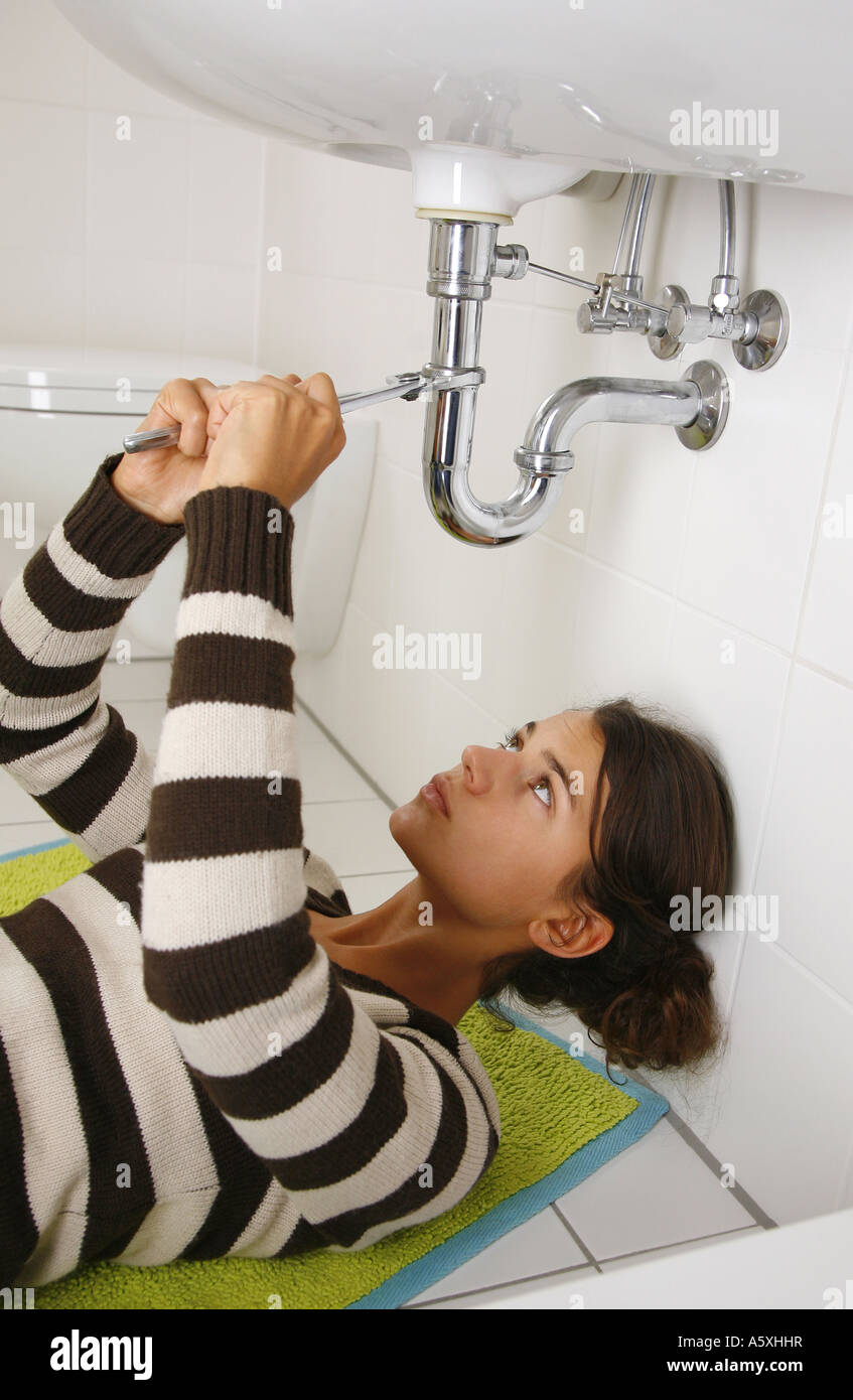 Young woman under bathroom sink fixing pipe Stock Photo Alamy