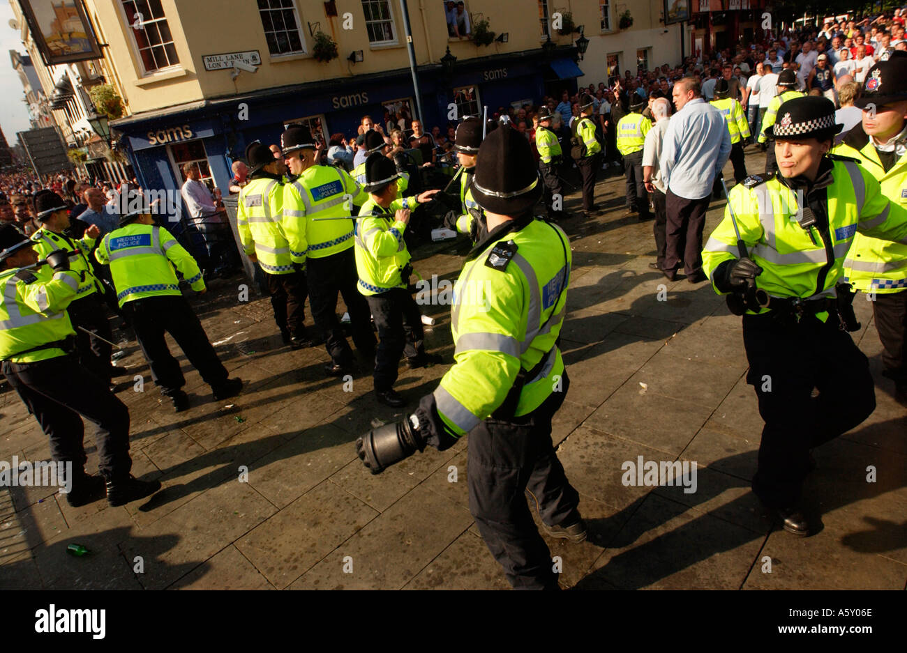 Police officers draw batons during trouble amongst football soccer fans drinking alcohol in Mill Lane Cardiff South Wales UK Stock Photo