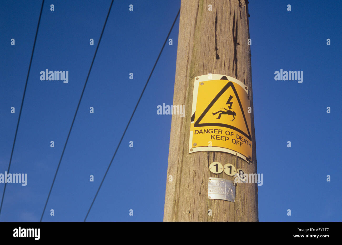 Yellow sign with iconic man being electrocuted and words Danger of death Keep off nailed over older sign on electricity pole Stock Photo