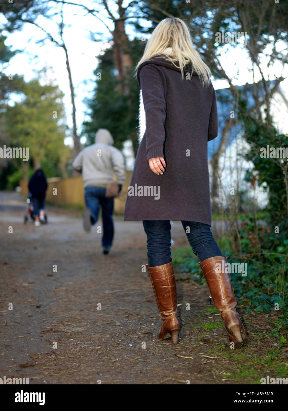 Young Woman Walking On A Quiet Public Path Being Threatened By A Mugging Robbery And The Threat Of Increasing Knife Crime By A Young Male Attacker Stock Photo