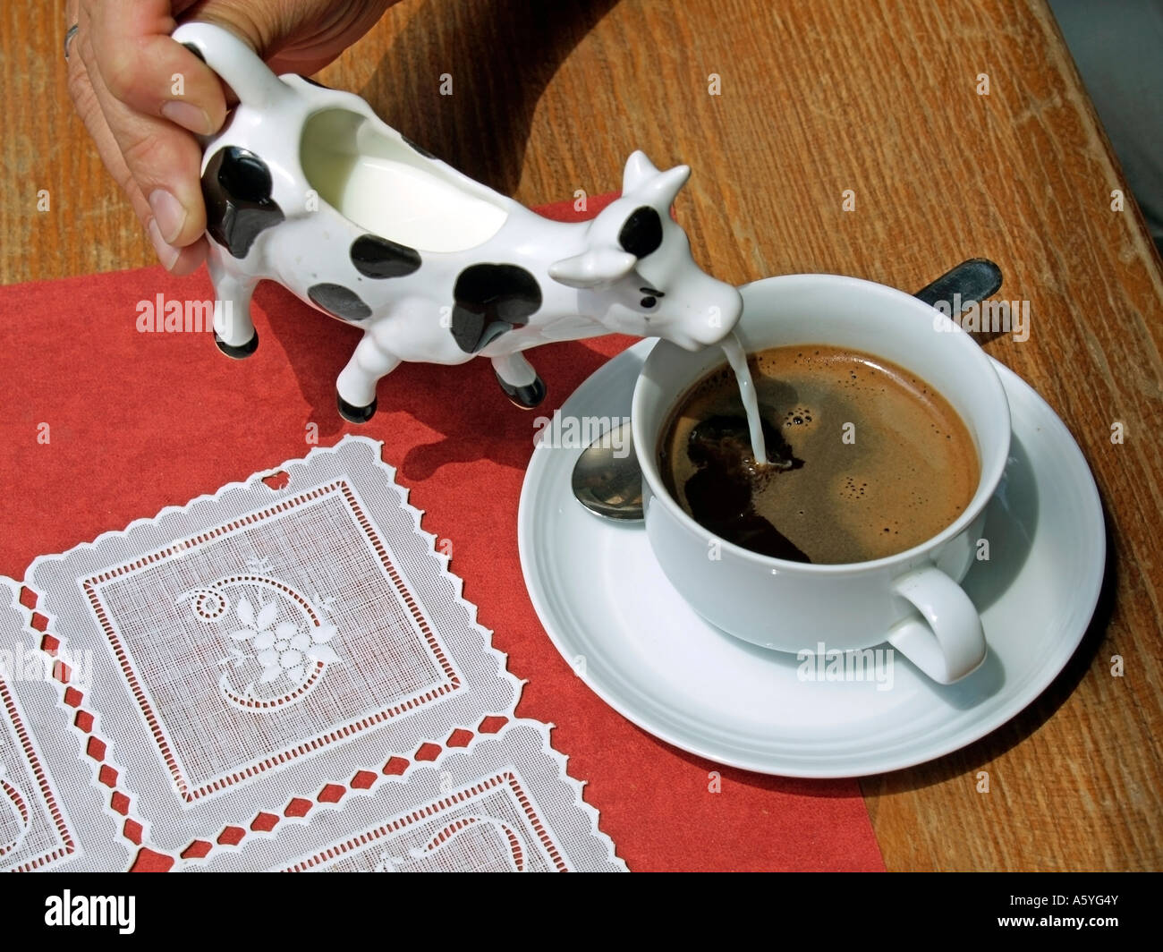 hand pouring milk out of a milk jug in form of a cow into a cup of