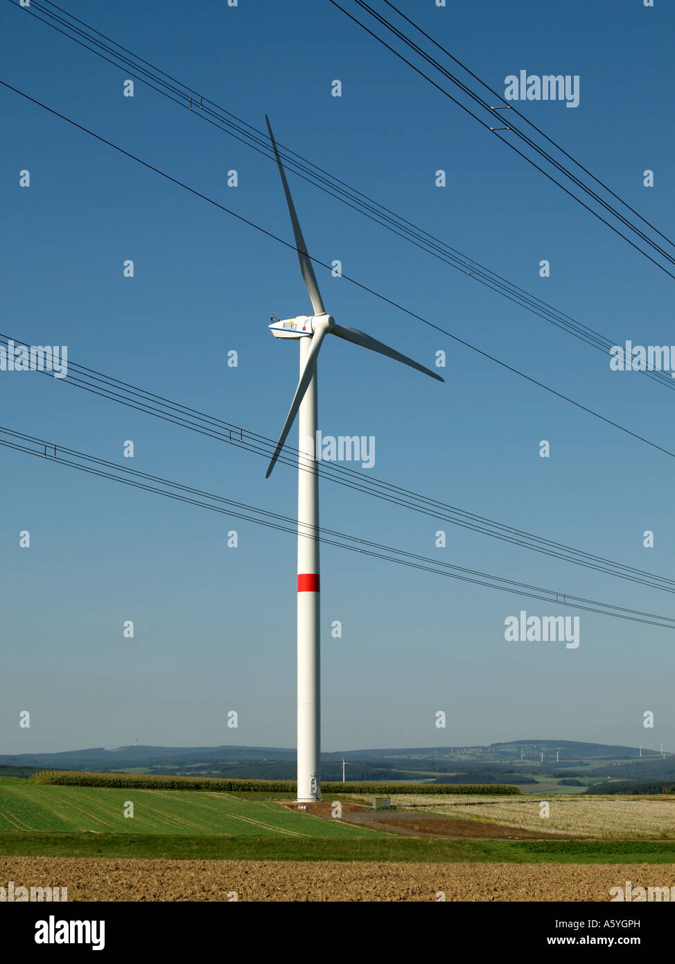 wind power station wind wheel behind power lines in country landscape of low mountain range Stock Photo
