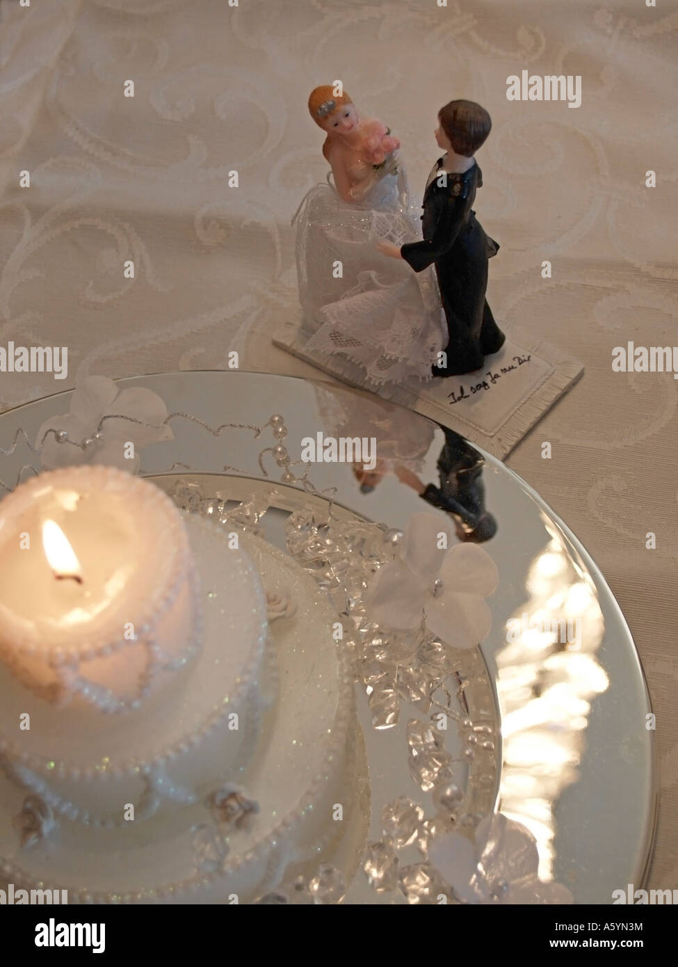 decoration for marriage little figures with bride and groom bridal pair beneath a burning candle on a table Stock Photo
