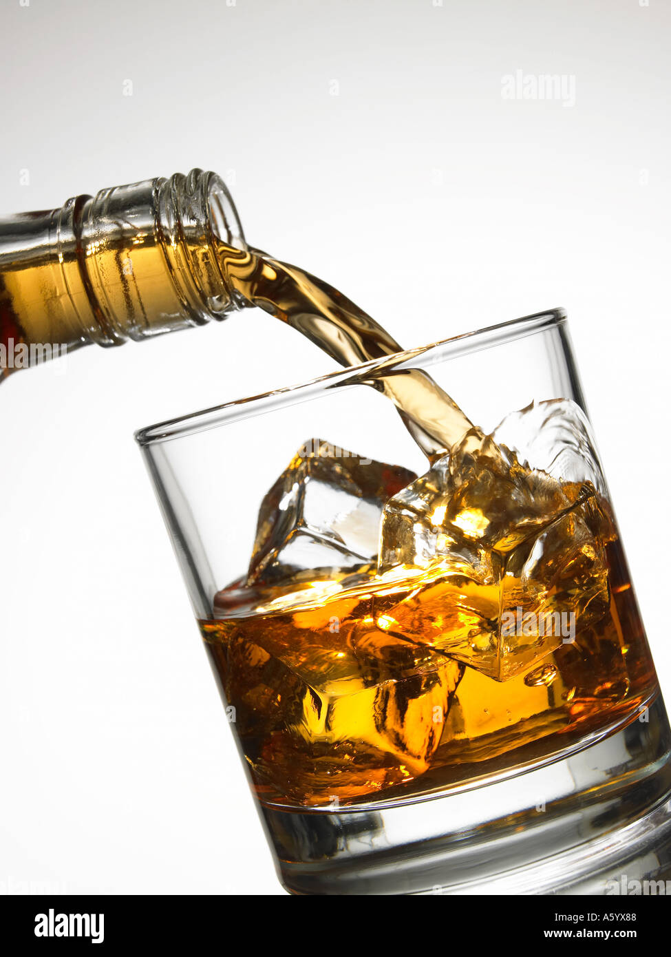 WHISKEY POURING FROM BOTTLE ONTO ICE CUBES IN GLASS TUMBLER Stock Photo