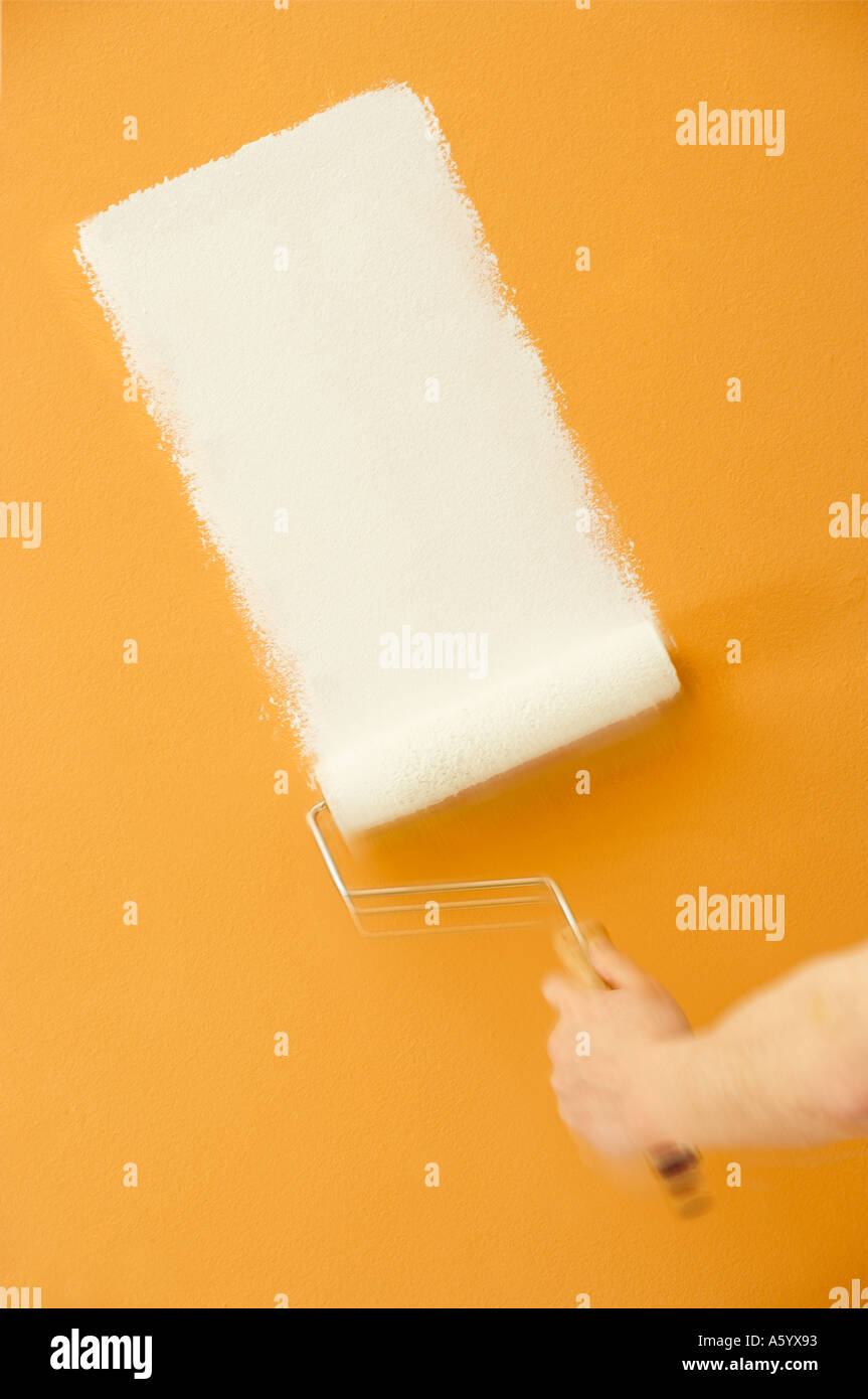 ROLLER APPLYING WHITE PAINT ON YELLOW WALL Stock Photo