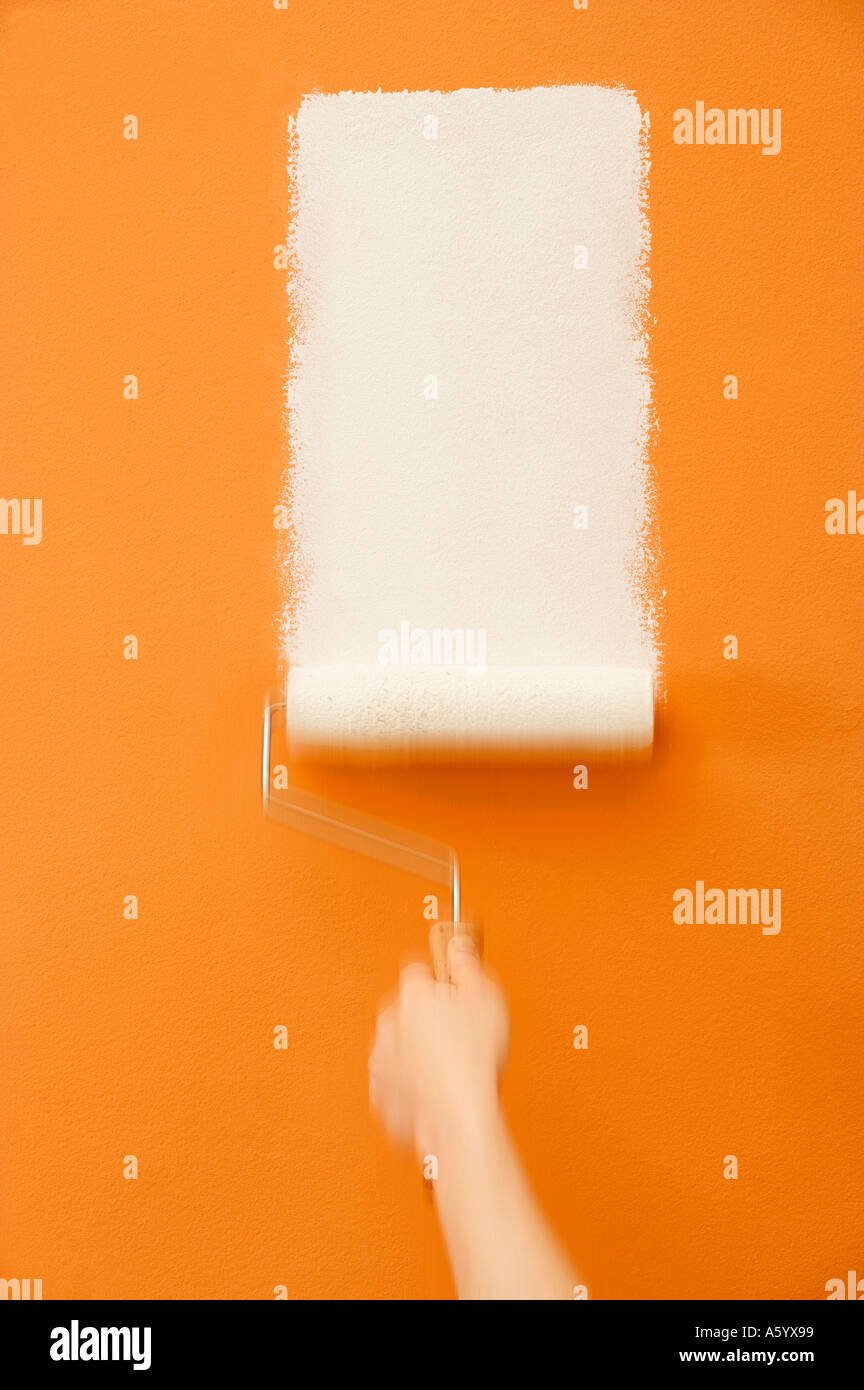 ROLLER APPLYING WHITE PAINT ON YELLOW WALL Stock Photo