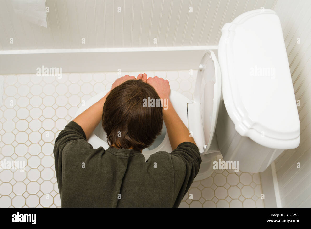 overhead view of male teenager bent over toilet being sick Stock Photo