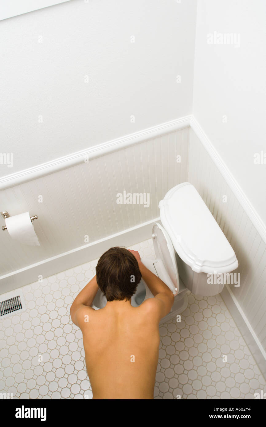 overhead view of shirtless male teenager bent over toilet being sick