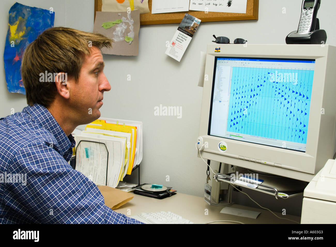male geophysicist working at computer with seismic record on screen Stock Photo